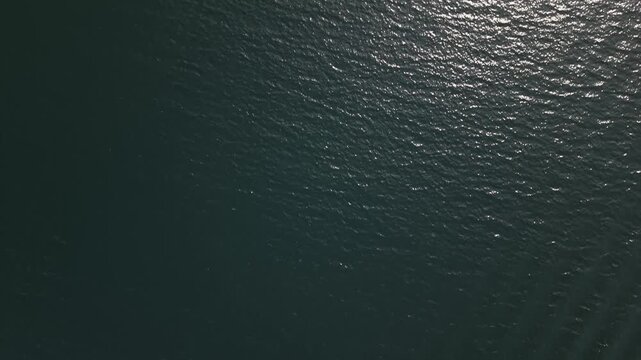 Top-down cinematic shot of the ocean surface, showing brilliant sunlight reflections scattered across small waves and creating a mesmerizing natural pattern.