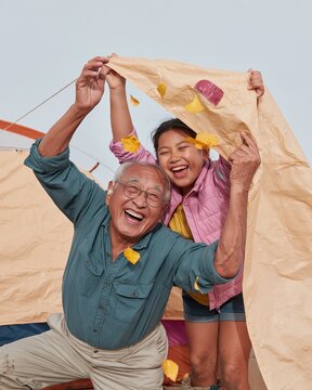 Family camping scene with a grandfather and granddaughter shaking wet autumn leaves off a tent fly sheet for tourism and outdoor insurance