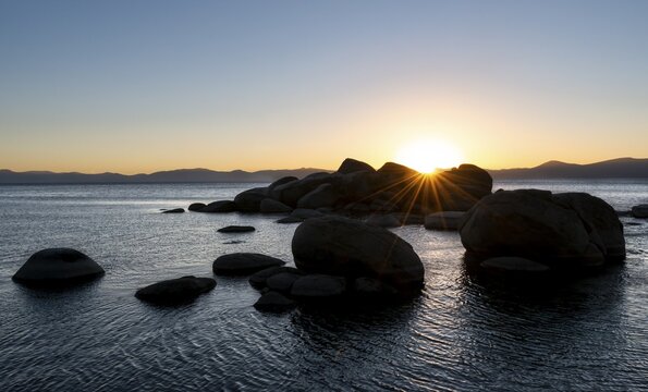 Sunset with sun star, round stones in the water, shore at Lake Tahoe, Sand Harbor State Park, shore, California, USA