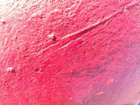 A tight close-up of a vivid red painted surface with a clear diagonal ridge or crack, small raised bumps, and a grainy, almost sandpaper-like texture under strong light.