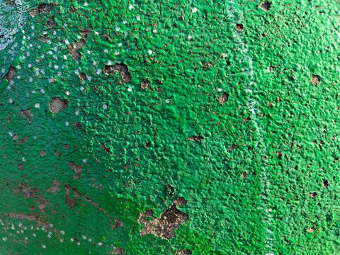 A bright green painted surface covered in dense fine cracks and scattered small holes that reveal the darker underlayer, creating a heavily weathered and textured appearance.