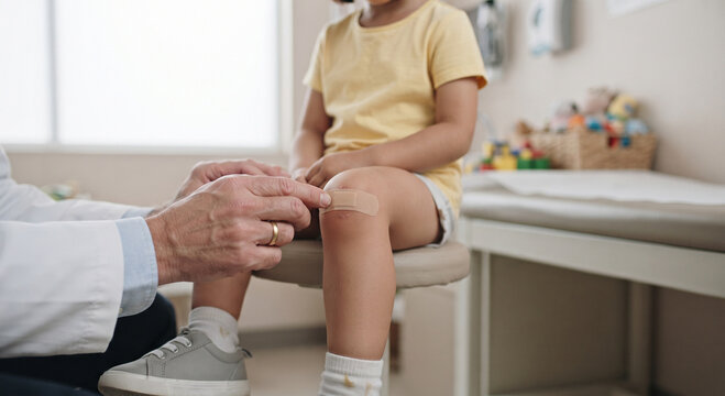 Doctor applying a plaster bandage to a young girl's scraped knee in a medical clinic