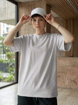 Short-haired woman wearing a grey baseball cap and plain t-shirt stands inside a contemporary building.