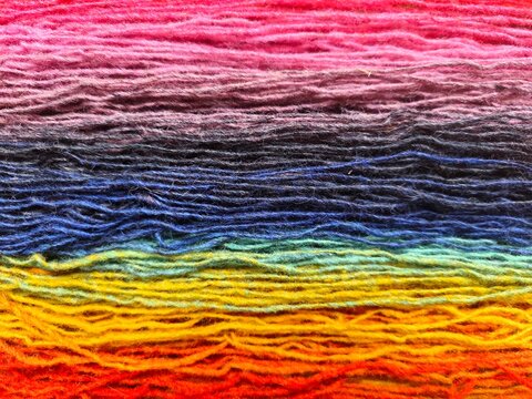 Full frame texture of colorful rainbow yarn threads for knitting and crafting. Bright multi-colored wool fiber background for handcraft, textile art, and needlework projects.