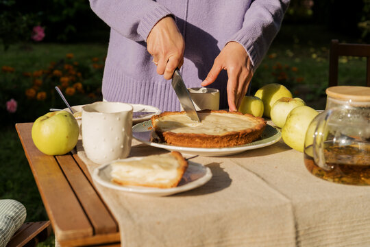 Woman hands slicing homemade apple pie at garden table close up