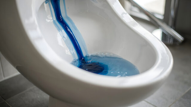 Blue liquid disinfectant pours down a white ceramic toilet bowl in a modern bathroom. Ideal for household hygiene and sanitary product advertising.