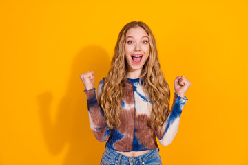 Fototapeta premium Young woman with blonde hair wears a tie dye top and celebrates with a smile against a bright yellow background
