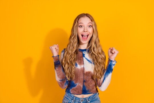 Young woman with blonde hair wears a tie dye top and celebrates with a smile against a bright yellow background