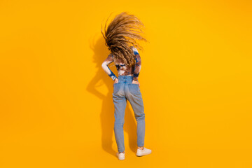 Naklejka na ściany i meble Young woman with flowing hair stands against a bright yellow background wearing jeans and a tie dye shirt