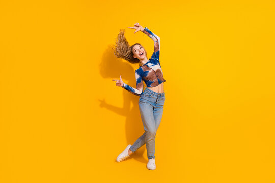 Young woman dancing in a tie dye top and jeans against a bright yellow backdrop showcasing energy style and joy