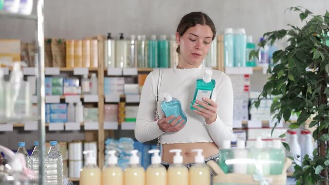 Young woman choosing a mint-flavored mouthwash against the background of shelves in a pharmacy . High quality 4k footage