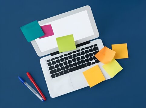 Top view flat lay of white laptop computer with colorful sticky notes and pens on dark blue background