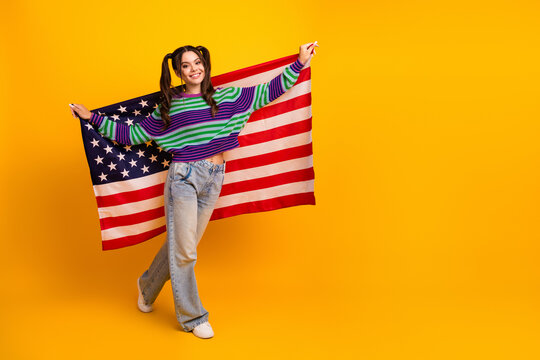 Young girl with American flag posing in bright yellow studio wearing striped sweater and jeans