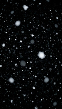 Snowflakes of different sizes falling on black background at night