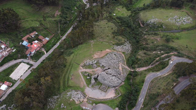 Aerial view of the Q'enqo archaeological site featuring ancient stone structures, rocky outcrops, and surrounding green landscape near the winding roads in Cusco, Cusco, Peru.
