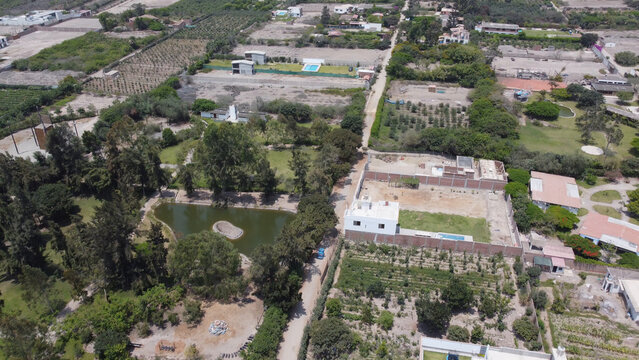Aerial view of the rural landscape of Azpitia, featuring lush green vegetation, a small pond, and scattered houses in Santa Cruz de Flores, Peru.