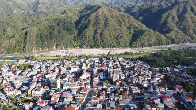 Aerial view of the town of La Merced nestled in the valley of the Andes mountains, featuring dense urban buildings, a winding river, and lush green mountain slopes in La Merced, Junin, Peru.