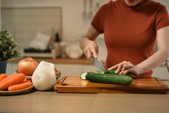 Cropped of Young Asian Woman Preparing Fresh Salad by Cutting Cucumber on Wooden Board in Modern Kitchen