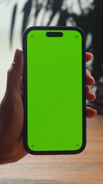 Phone with green screen in hand, close up of smartphone chroma key mockup, man holding mobile phone with blank green display, app template, copy space on table