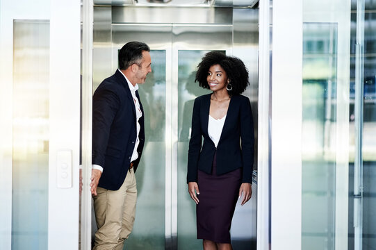 Business, people and leaving elevator in office for work arrival, enter building and employee respect. Woman, man and holding lift door with courtesy for exit, company floor or walking to appointment