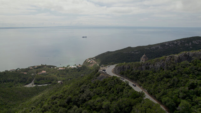 Aerial view of Serra da Arrabida with a winding coastal road, lush green hills, and the Atlantic Ocean in the background in Sao Lourenco, Setubal, Portugal.