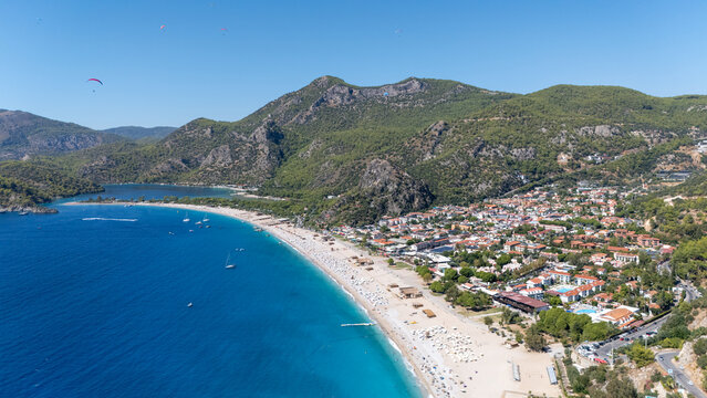 Aerial view of the famous Oludeniz beach and lagoon, featuring turquoise waters, sandy coastline, paragliders in the sky, and surrounding green mountains in Oludeniz, Mugla, Turkiye.