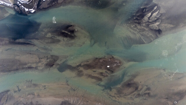 Aerial view of the glacial river delta near Vestrahorn with intricate sediment patterns, turquoise water channels, and dark volcanic sand deposits in Hofn, Sveitarfelagid Hornaf, Iceland.