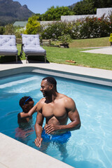 Naklejka premium African American father and youth playing in backyard pool, father wearing blue trunks, goggles