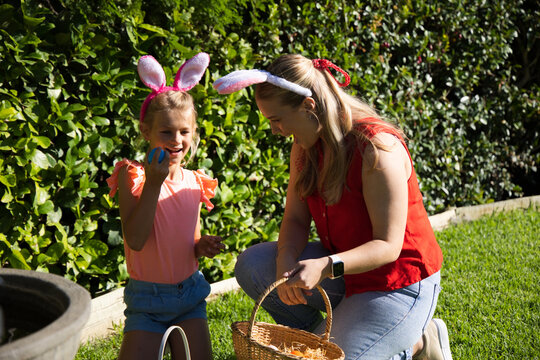 Mom and daughter wearing bunny ears celebrating in garden holding woven basket with eggs