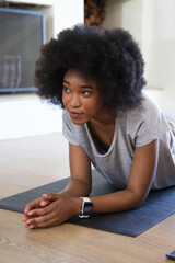 Naklejka premium Female holding forearm plank, looking left on dark mat in living room with smartwatch