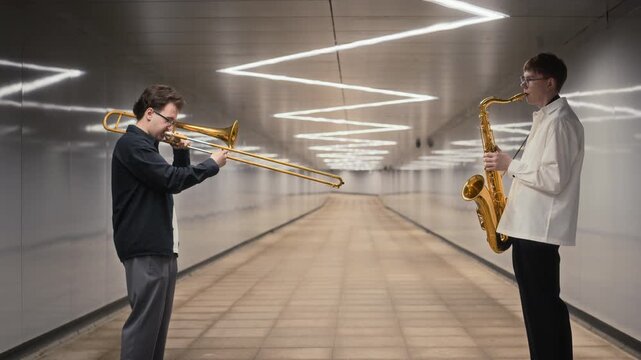 Caucasian young adults playing trombone and saxophone in pedestrian subway tunnel. Clip suits urban culture campaigns, music education projects, and creative performance promotions