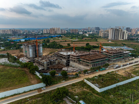 Aerial view of a large construction site featuring multiple buildings in progress with cranes, surrounded by greenery and urban development in Gurugram, Haryana, India.