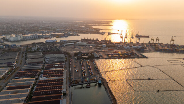 Aerial view of Pelabuhan Tanjung Emas port facilities with shipping containers, cranes, and warehouses along the coastline at sunset in Semarang Utara, Central Java, Indonesia.