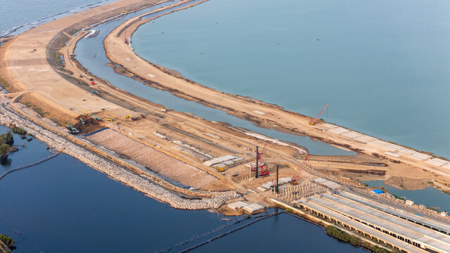 Aerial view of the construction site at Pelabuhan Tanjung Emas with cranes, earthworks, and coastal infrastructure along the sea in Semarang Utara, Central Java, Indonesia.