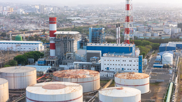 Aerial view of the Pelabuhan Tanjung Emas power plant featuring large industrial storage tanks and tall chimneys in the port area of Semarang Utara, Central Java, Indonesia.
