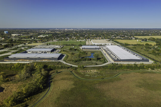Aerial view of a data center complex featuring industrial buildings, rooftop cooling units, a small pond, and surrounding grassy fields in Hoffman Estates, Illinois, United States.