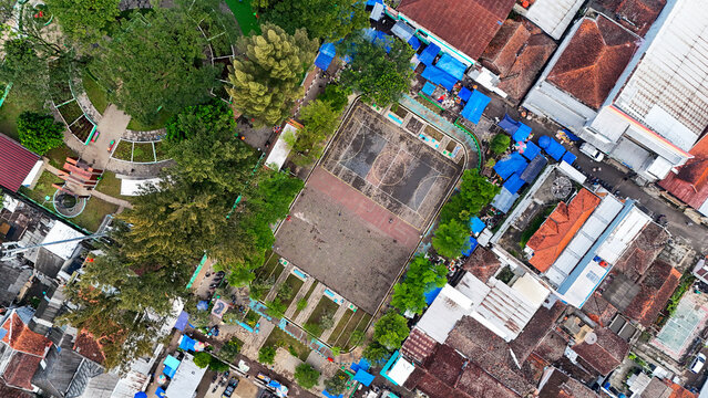 Aerial view of Ciwidey public square featuring a sports court surrounded by dense urban buildings, lush trees, and market stalls in Bandung, West Java, Indonesia.