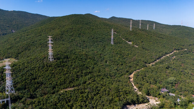 Aerial view of Jangsan mountain covered in dense green forest with high-voltage electricity transmission towers standing along the ridge under a clear blue sky Busan, Busan, South Korea.