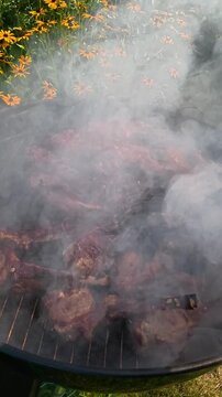 Portioned lamb chops (rack of lamb) are grilling on the grate of a round charcoal grill.