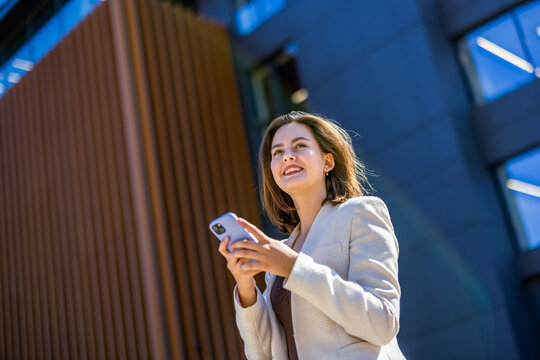 Low angle view of smiling businesswoman texting on smartphone outside business center