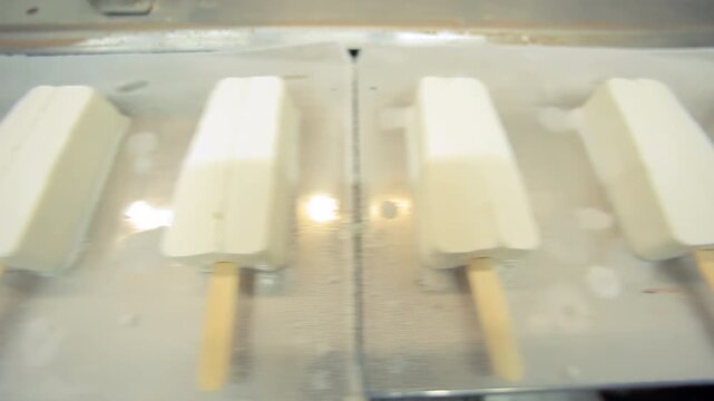 Popsicle factory production line closeup. White ice cream bars wooden sticks.