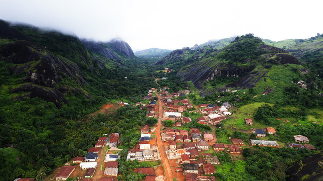Aerial view of Idanre town nestled between dramatic, dark, rounded rock formations of the Idanre Hills, with lush vegetation, a dirt road, and houses in Idanre, Ondo, Nigeria.
