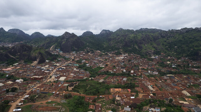 Aerial view of the historic town of Idanre nestled among dramatic rocky peaks, featuring dense residential housing with brown rooftops and lush vegetation in Idanre, Ondo, Nigeria.