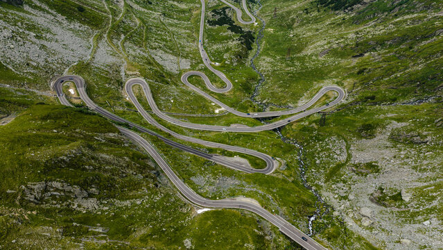 Aerial view of the Transfagarasan mountain road with its iconic hairpin turns winding through the lush green Fagaras Mountains in Cartisoara, Sibiu, Romania.