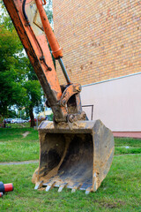 Orange Excavator Bucket on Grass Ground at Urban Construction Site Concept © yaviki