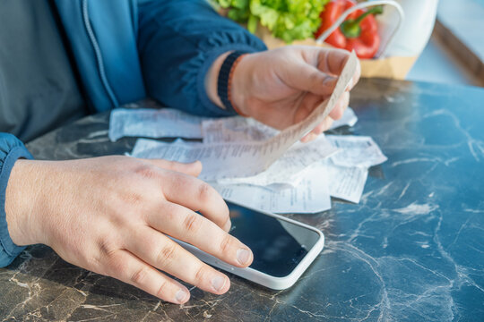 Man uses smartphone calculator to add up grocery expenses from several long shopping receipts after buying food. Household budgeting, expense calculation, food inflation, rising grocery prices