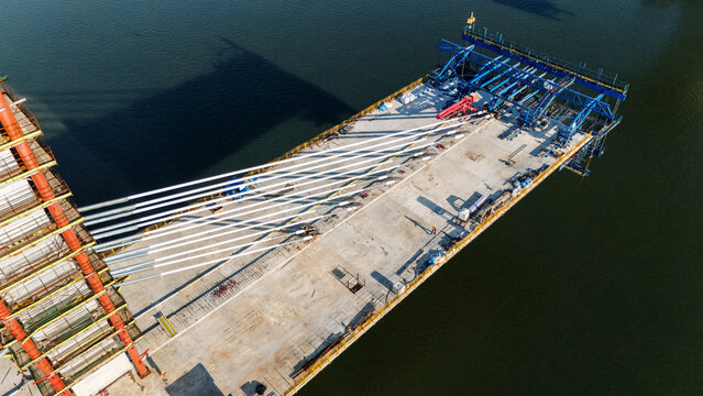 Aerial view of a cable-stayed bridge under construction with steel cables extending from the pylon to the concrete deck over the river in Novi Sad, Vojvodina, Serbia.