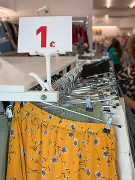 Closeup of clear 1 euro price sign inside thrift store and second hand clothes on hangers. Affordable used fashion, reuse, budget shopping. Sustainability, circular economy, zero waste, thrift concept