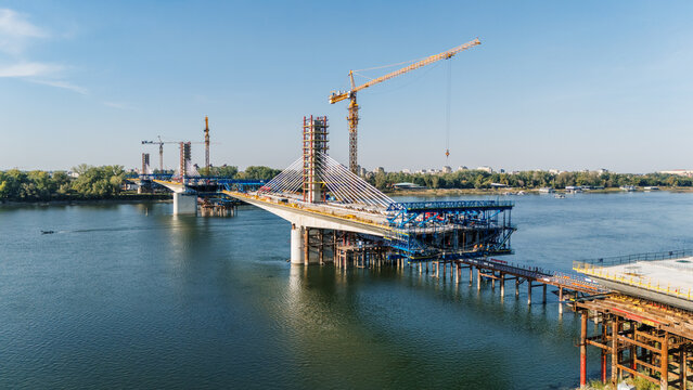 Aerial view of the Zezelj Bridge under construction over the Danube river with tall cranes and steel structures in Novi Sad, Vojvodina, Serbia.