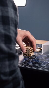 Architect hand placing miniature wooden building model onto urban master plan layout for city development project